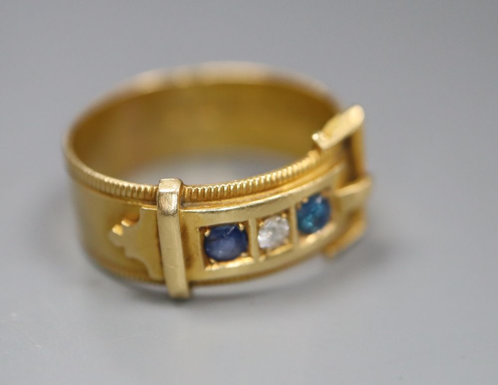 A late Victorian 18ct gold, three stone sapphire and diamond set buckle ring, size O/P, gross 5.1 grams.